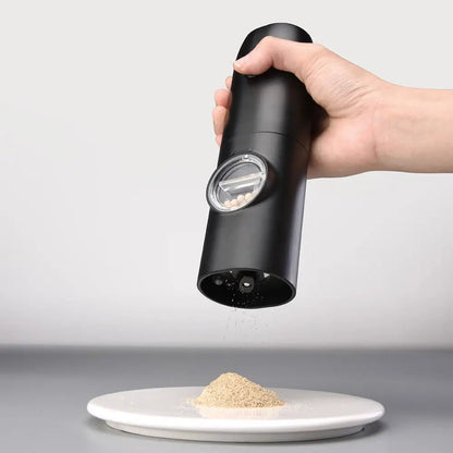 Hand using electric salt and pepper mill to grind seasoning onto a white plate, with peppercorns visible through transparent window.