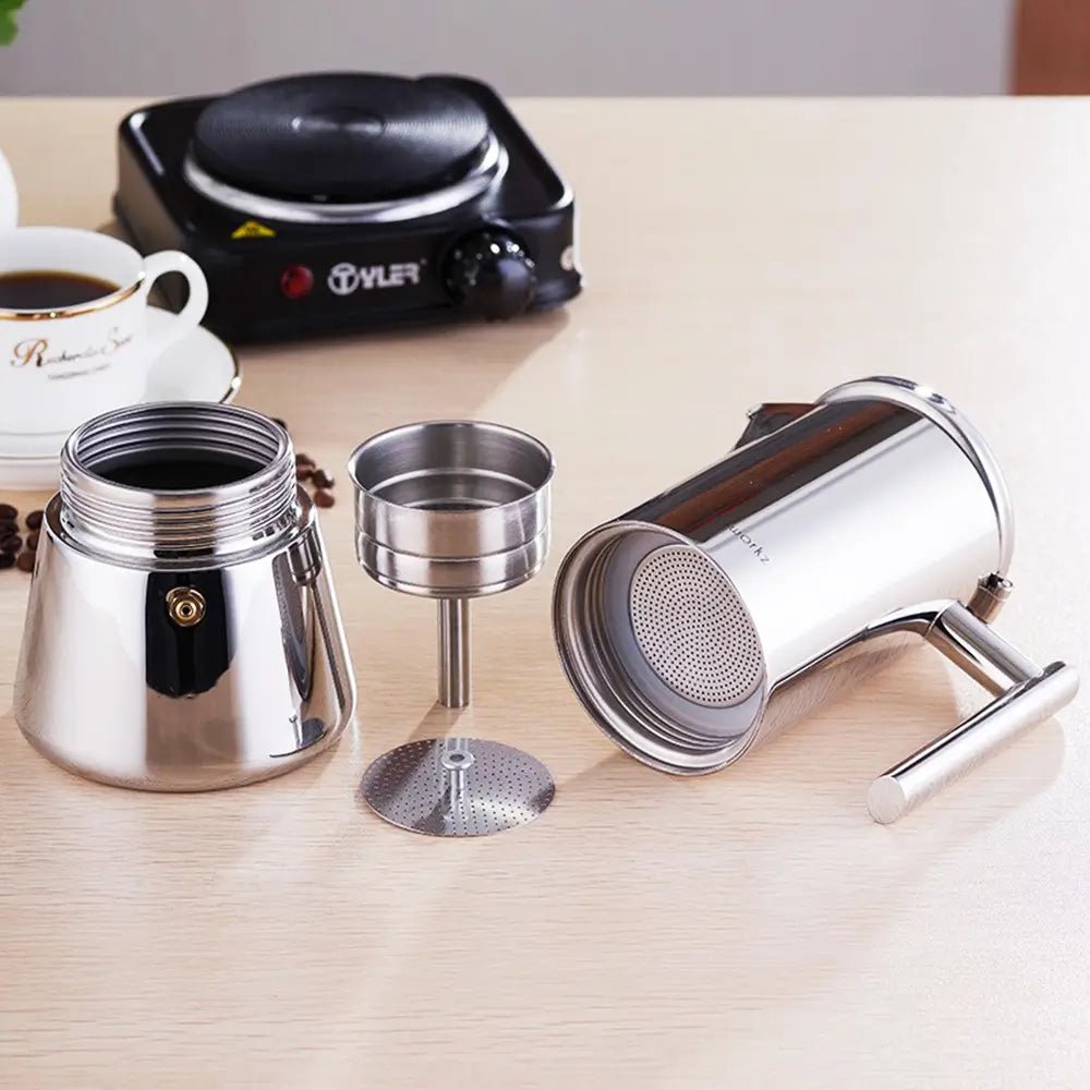 Disassembled stainless steel stovetop espresso maker with boiler, funnel, filter plate, and coffee container on a table.