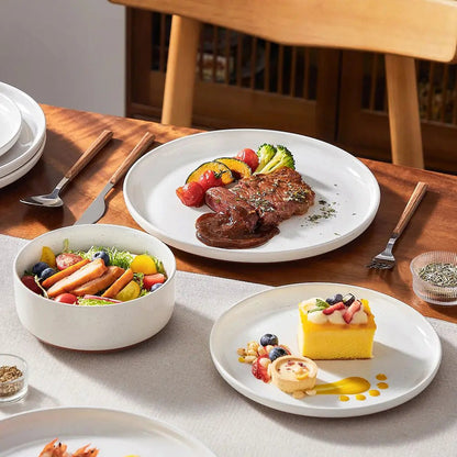 Everyday stoneware dinnerware sets with plates and bowls serving steak, salad, and dessert on a wooden dining table.
