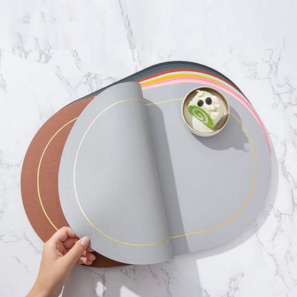 Faux leather placemats in assorted colors, shown stacked with a hand lifting the top gray mat, placed on a marble table with a dessert plate.