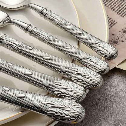 Flatware collections with textured silver handles featuring wheat details, placed over white plates on a soft textured surface.