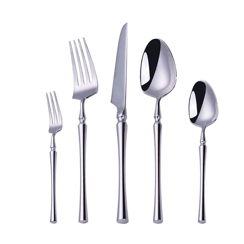 Elegant flatware place setting with gold and silver stainless steel utensils on a dark table, paired with plates and tomatoes.