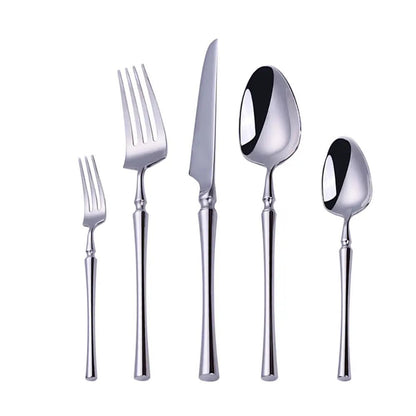 Elegant flatware place setting with gold and silver stainless steel utensils on a dark table, paired with plates and tomatoes.