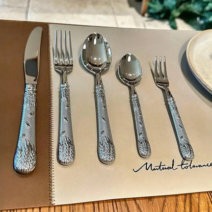 Set of polished silver flatware with textured floral handles neatly arranged on a neutral placemat beside a ceramic plate.