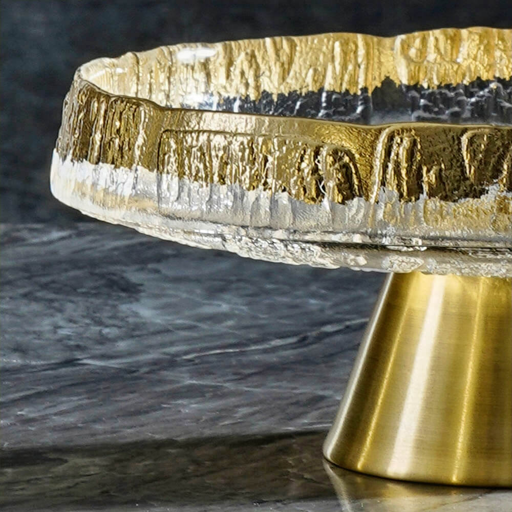 Close-up view of a luxurious footed glass fruit bowl featuring a textured gold and silver rim that adds a touch of sophistication. The sturdy brass-tone base enhances its modern design, making it an elegant centerpiece for displaying fruits or desserts.