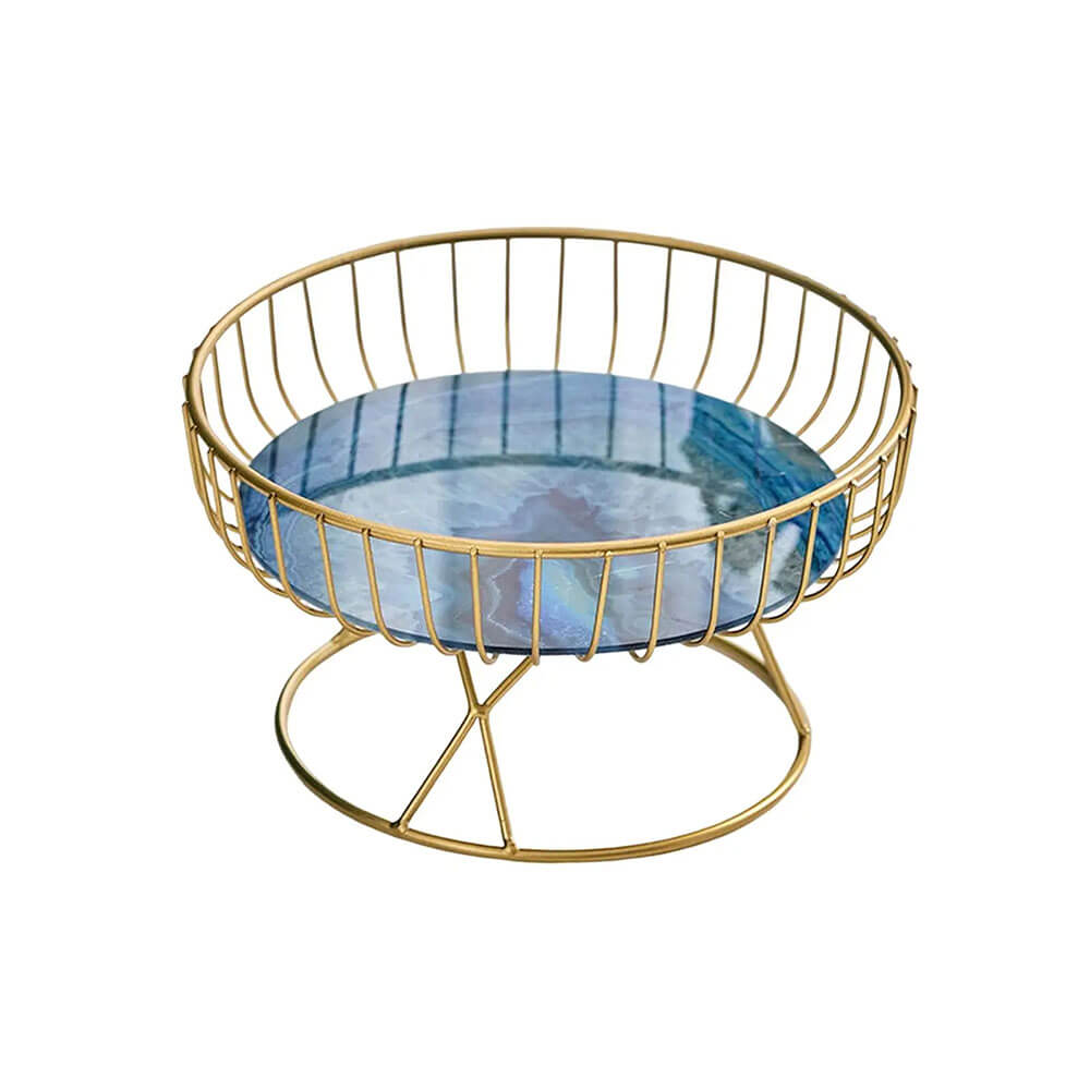 A modern pedestal fruit bowl with a round blue marble base featuring intricate natural patterns, surrounded by a gold metal wire frame and supported by a gold pedestal stand for a luxurious aesthetic.