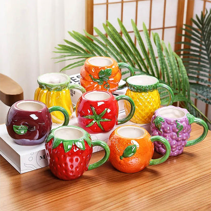 A group of vibrant fruit mugs featuring pumpkin, orange, grape, tomato, strawberry, pineapple, and banana designs with ergonomic handles and premium ceramic finish.