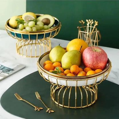 Decorative pedestal fruit bowl with ceramic dish and gold wire base, filled with apples, pears, grapes, and citrus on table.