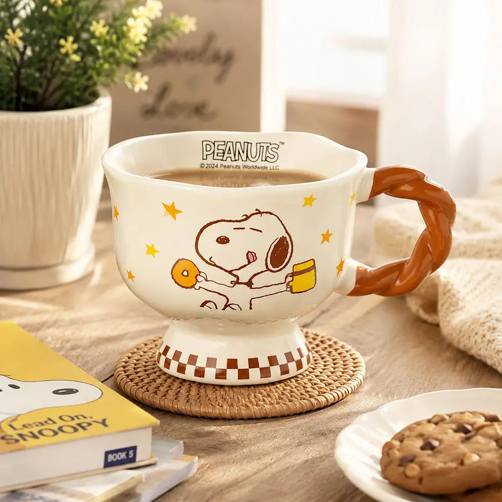 Cartoon coffee mug filled with coffee on a woven coaster beside a cookie, books, and a potted plant on a wooden table.