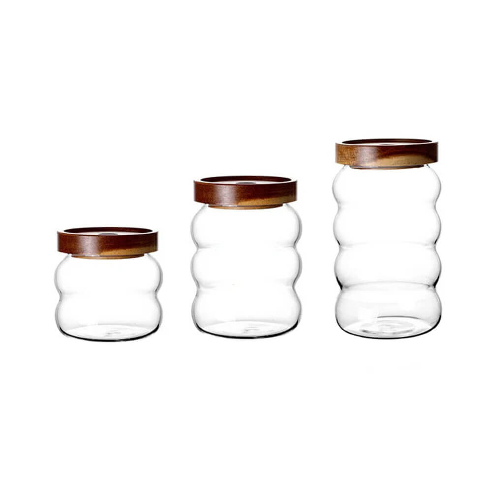 Minimalist glass canister set featuring three clear ripple-textured glass jars with dark wooden lids, displayed in small, medium, and large sizes on a white background.