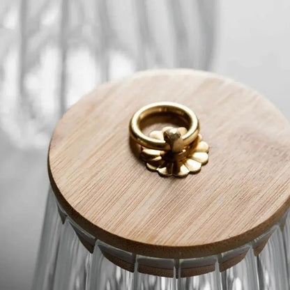 Glass container with a wooden lid featuring a gold bee design on a neutral background.