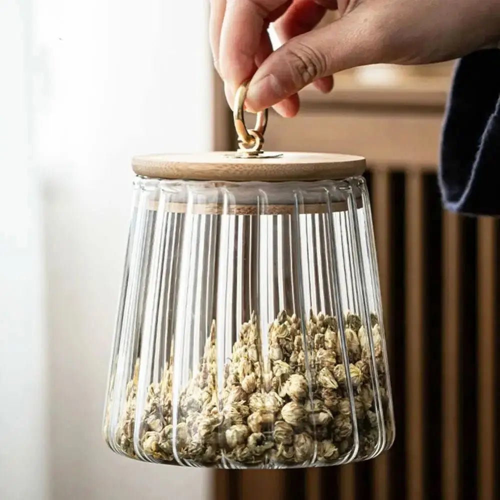 Glass container with wooden lid held by a hand, filled with dried herbs.