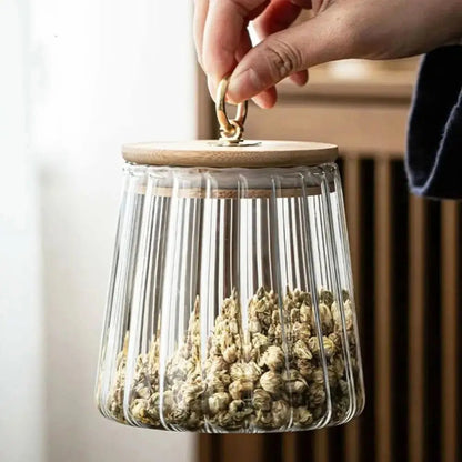 Glass container with wooden lid held by a hand, filled with dried herbs.