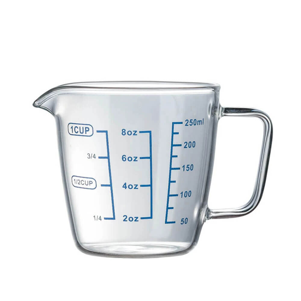 A clear glass measuring cup with blue measurement markings for ounces, cups, and milliliters, featuring a curved spout and a sturdy handle.