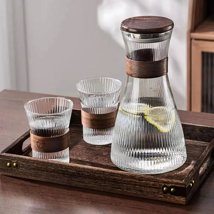 Glass pitcher set with ribbed surface, wooden lid, two ribbed glasses with wooden bands, placed on wooden tray.