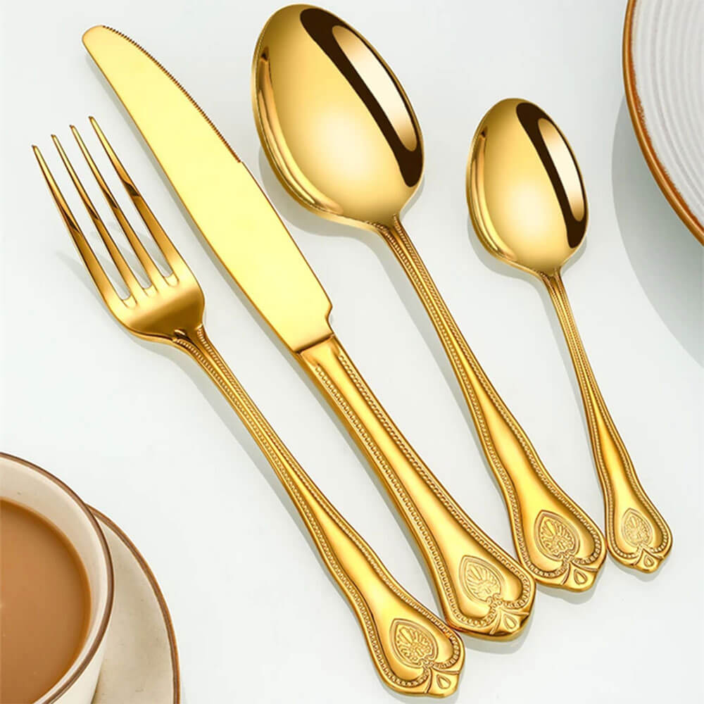 Gold flatware set with ornate, embossed handles placed beside a cup and plate on a white surface.
