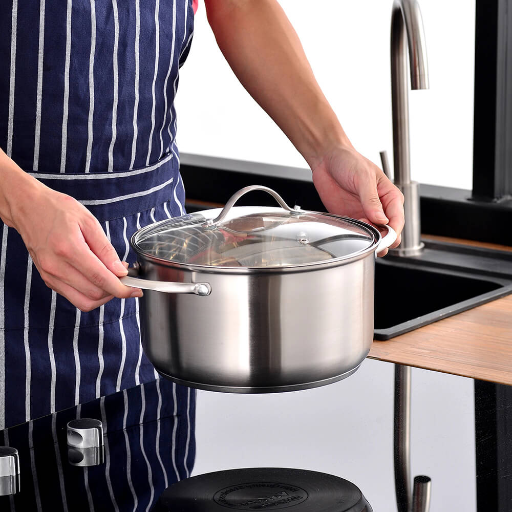 A person holding a shiny stainless steel pot with a glass lid in a modern kitchen showcasing a durable and stylish option from good stainless steel cookware sets.