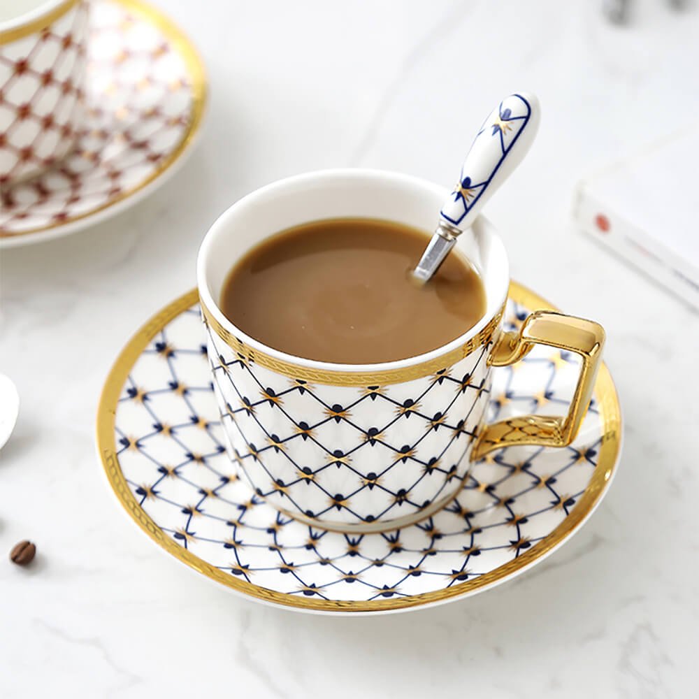 A close-up of a luxurious honeycomb tea set pack, featuring a bone china cup with an intricate blue honeycomb pattern, golden accents, and a matching saucer. A stylish spoon rests inside the cup filled with tea, showcasing elegance and craftsmanship.