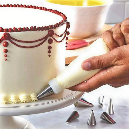 A person decorating a white frosted cake using an icing bag and a stainless steel nozzle, creating a detailed cream border at the base. The cake also features intricate red icing designs along the top edge. Several stainless steel nozzles are placed on the table nearby, showcasing the versatility of the icing bag and nozzle set for cake decoration.