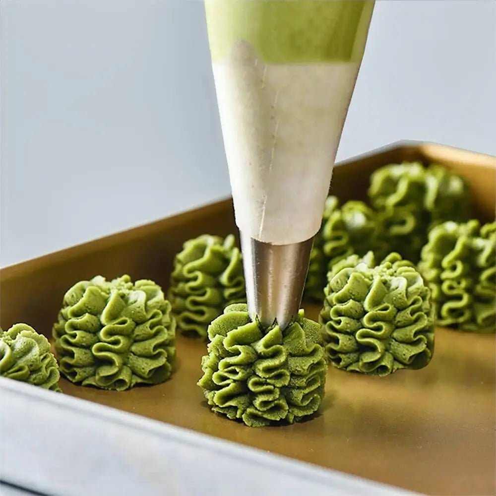 Close-up of icing set cake decorating tool piping green frosting designs onto a baking tray with multiple finished decorations.