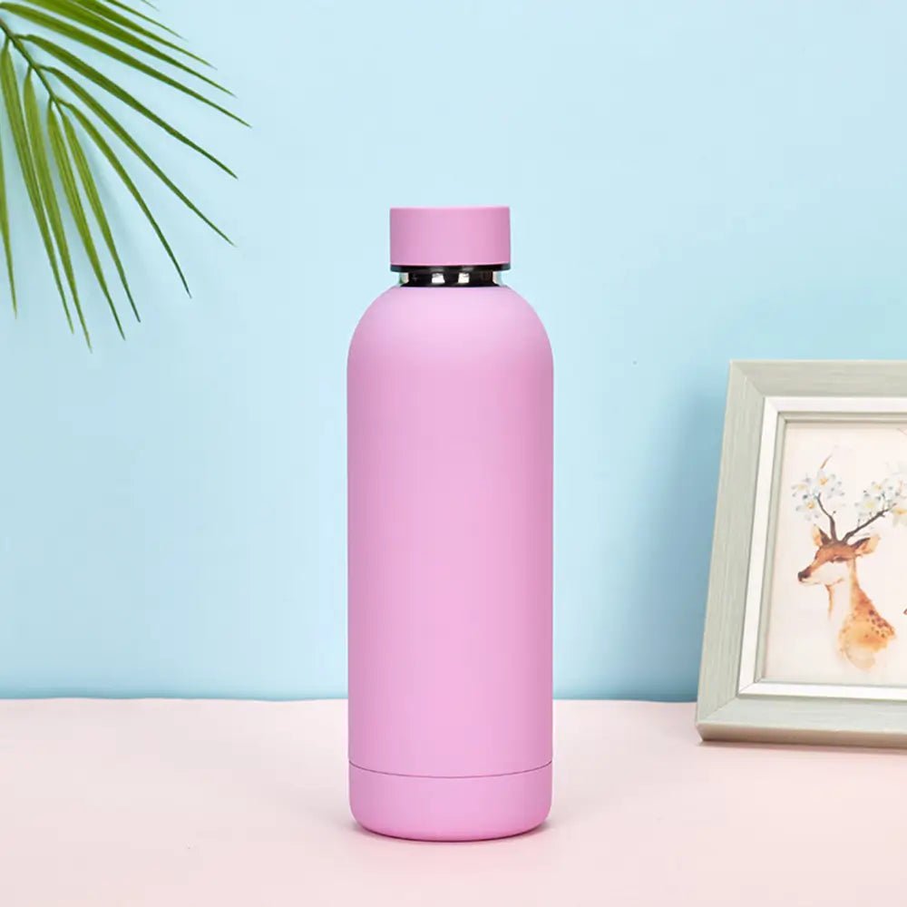 Pink water bottle on a pink surface with a light blue background and a framed picture of a deer.