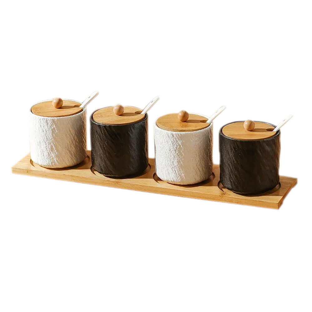 A kitchen canister set consisting of four ceramic jars with a textured finish, alternating in black and white. Each jar has a bamboo lid with a wooden knob and a slot for a small white spoon. The jars are neatly arranged on a rectangular bamboo tray, offering a clean and functional design.