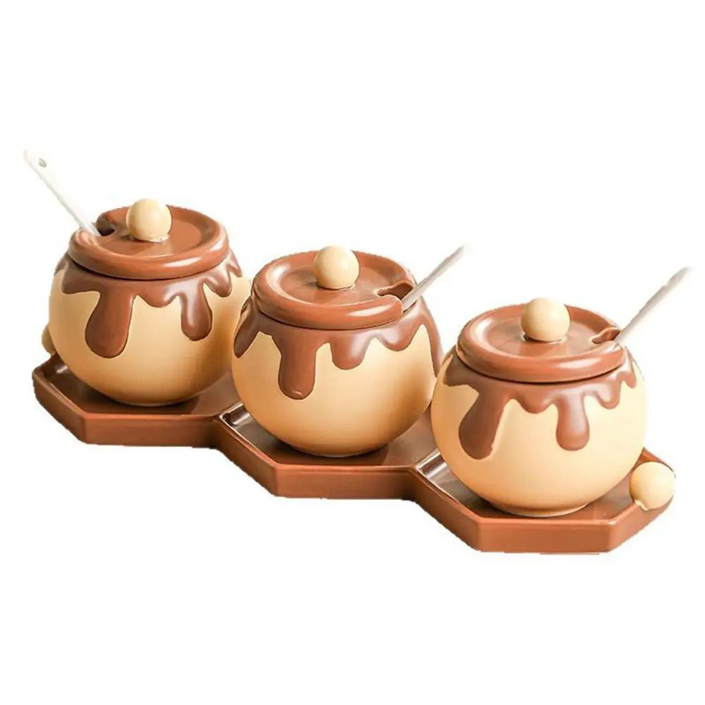 A three jar kitchen canister set featuring round ceramic containers with chocolate-drip lids, matching spoons, and a connected brown tray.