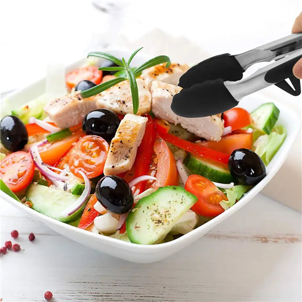 Greek salad with chicken, olives, and vegetables in a white bowl with silicone tongs.
