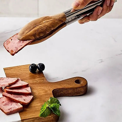 Wooden cutting board with sliced meat and a hand using tongs to pick up a slice.