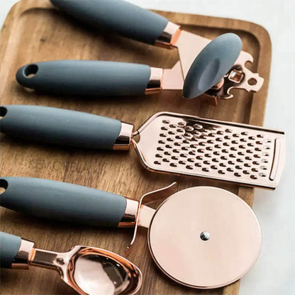 A premium kitchen tool set crafted with stainless steel and copper accents, featuring elegant matte gray handles, including a grater, pizza cutter, ice cream scoop, and can opener, displayed on a wooden serving board for a sophisticated kitchen aesthetic.