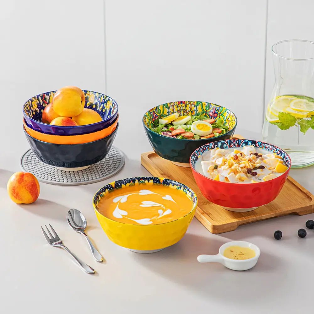 Colorful ceramic large serving bowl set with food, including soup, salad, fruit, and dessert, displayed on a dining table.