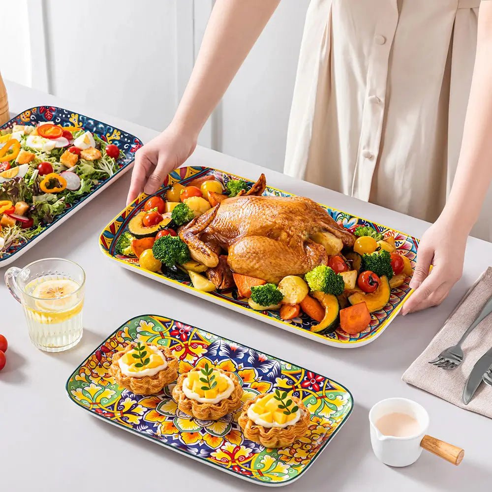 Large serving plate with colorful floral design holding roasted chicken and vegetables on a dining table with other food.