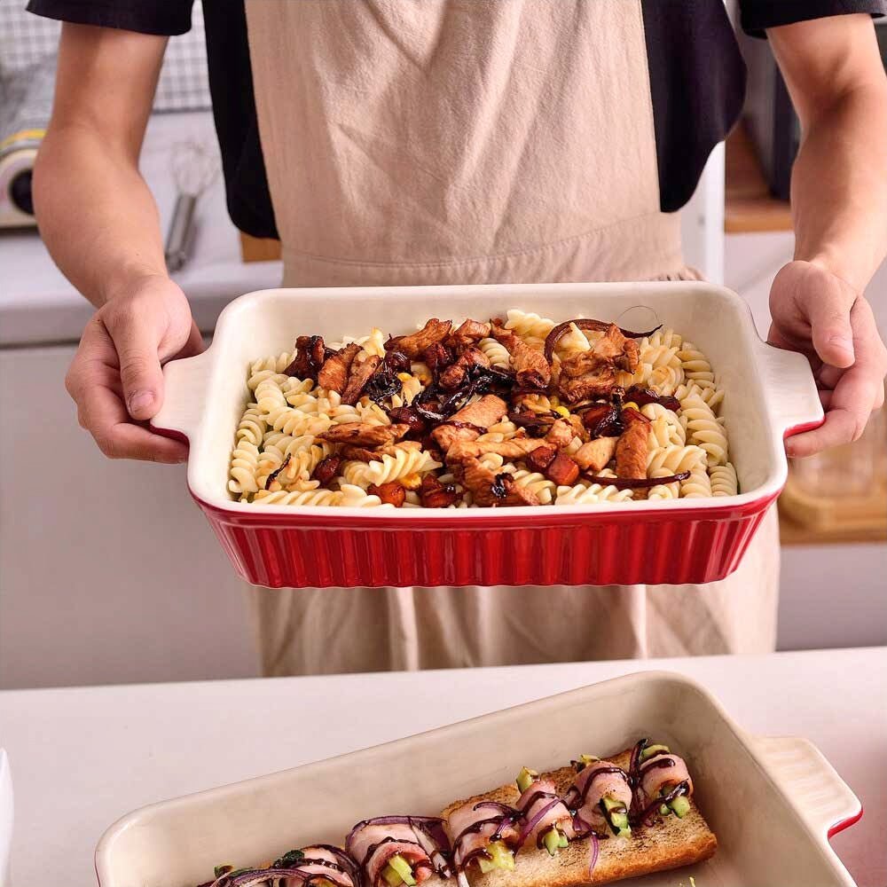 A woman holding a Le Creuset baking dish filled with cooked pasta and vegetables.