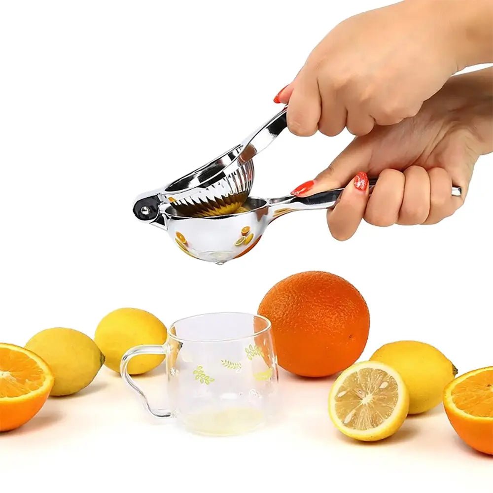 Hand pressing a stainless steel lemon squeezer over a glass, surrounded by fresh lemons and oranges on a white background.