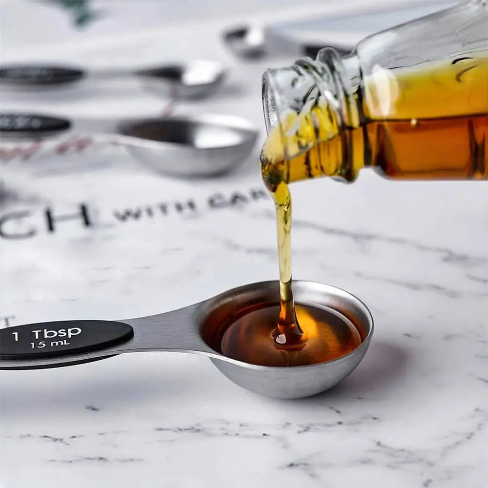 Bottle pouring liquid into a metal measuring spoon on a marble surface with a magazine in the background.
