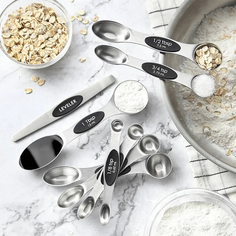 Set of stainless steel measuring spoons with black labels on a kitchen counter with ingredients.