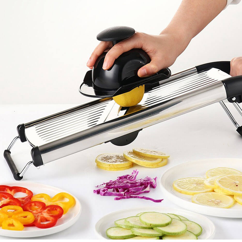 Mandolin vegetable slicer cutting lemon slices with safety holder, surrounded by sliced peppers, cabbage, and cucumbers.
