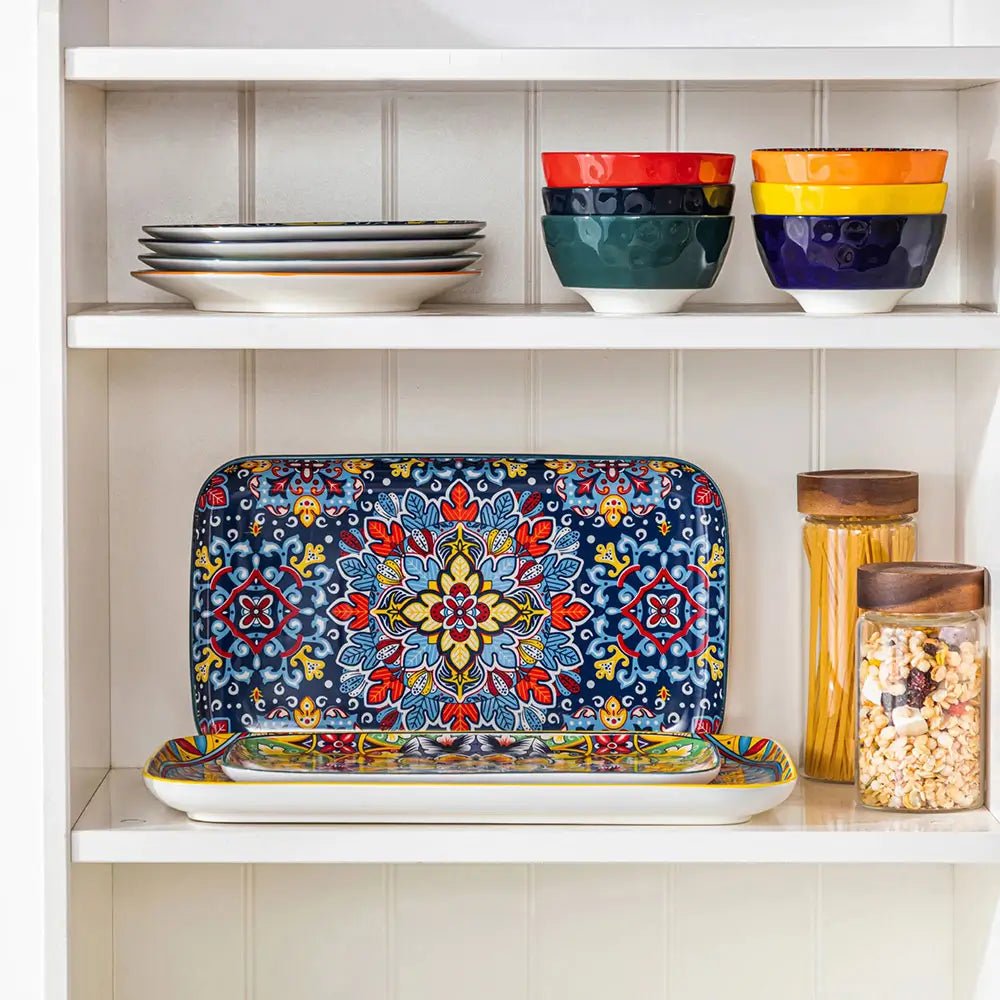 Modern serving plates with colorful floral and geometric patterns displayed on a kitchen shelf beside bowls, plates, and jars.