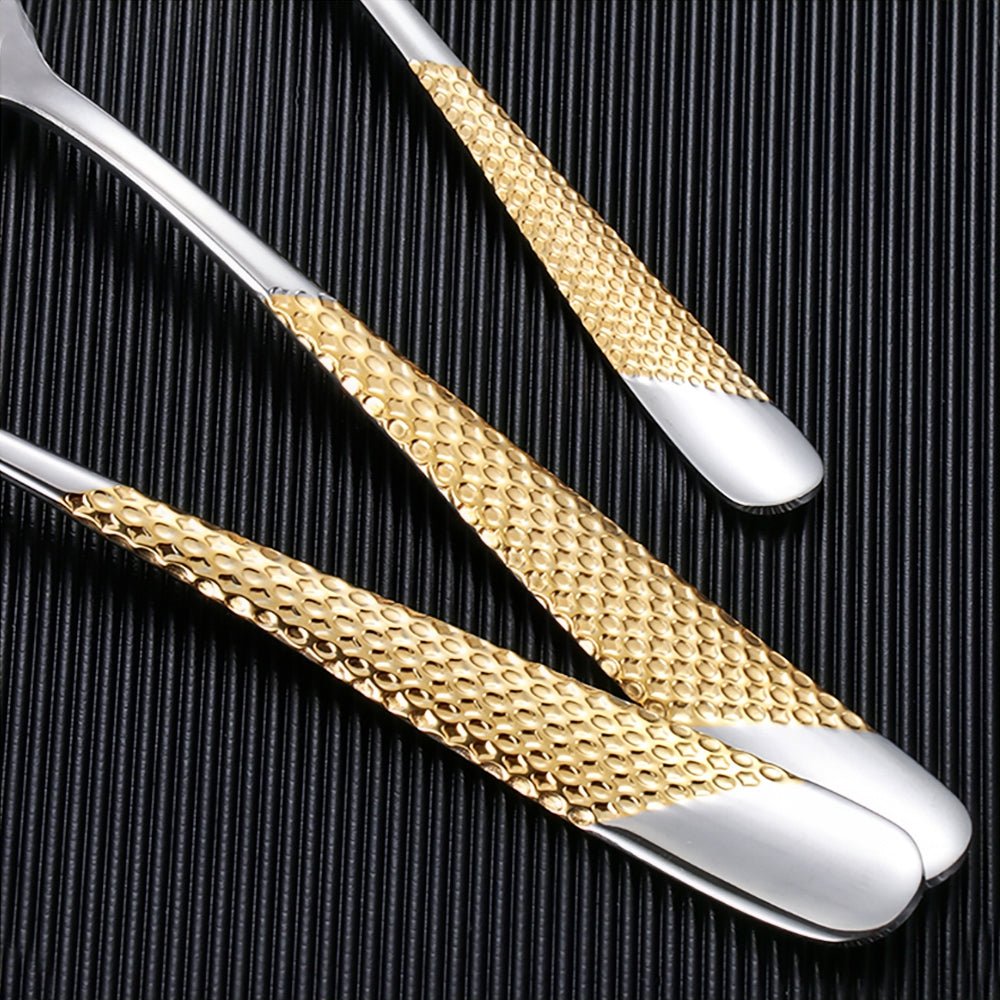 Close-up of stainless steel flatware with textured gold handles on a black ribbed surface.
