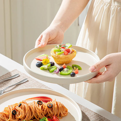 A woman holding a salad plate full of dessert and fruits and another dinner plate with pasta and red sauce on the dining table from the modern stoneware dinnerware set.