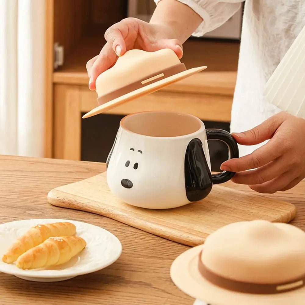 Person holding a dog-shaped mug with a lid on a wooden table.