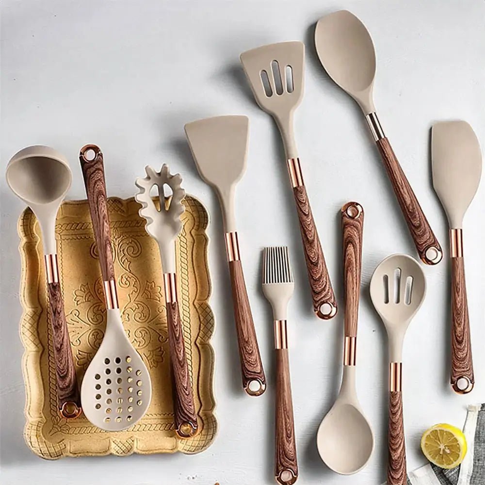 Beige silicone non stick cooking utensils with wood grain handles and copper accents displayed on a white surface with a lemon slice.