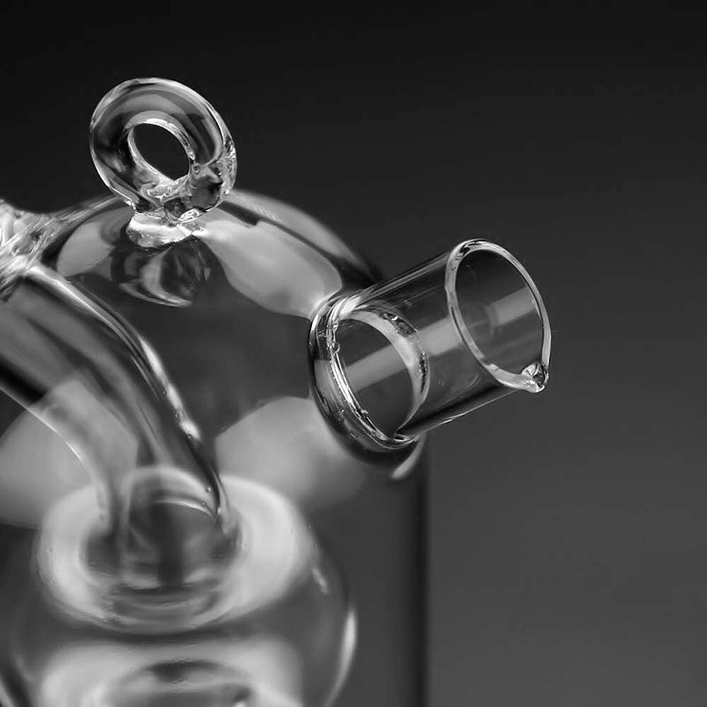 Close-up of a glass oil and vinegar bottle, highlighting the precision-pour spout and dual-chamber design. The transparent glass construction showcases the elegant craftsmanship, set against a dark background.