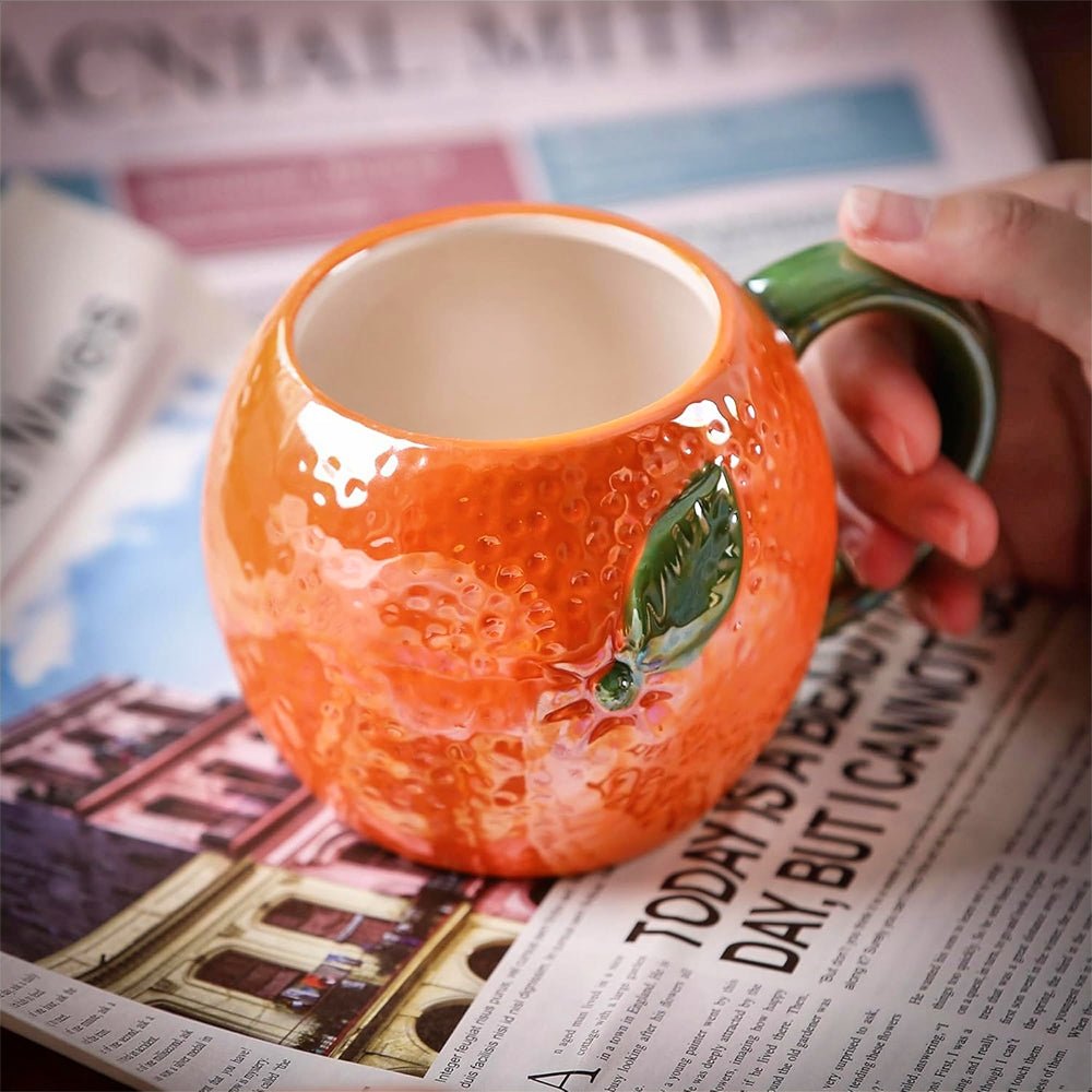 A woman holding a vibrant orange-shaped coffee mug with a detailed fruit design and ergonomic handle.