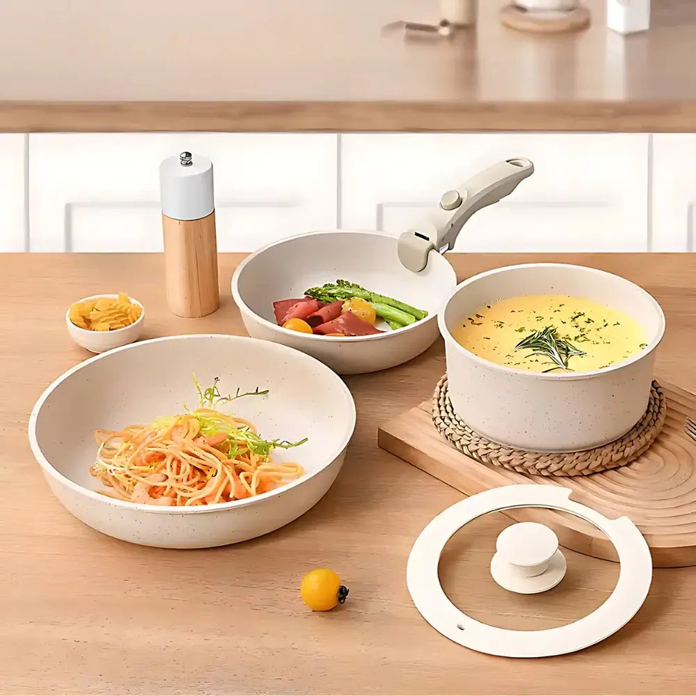 Pan set with removable handles on a wooden table, one pan with pasta, one with soup, one with vegetables, and a glass lid nearby.