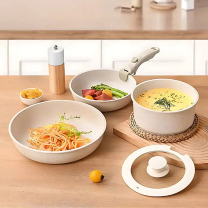 Pan set with removable handles on a wooden table, one pan with pasta, one with soup, one with vegetables, and a glass lid nearby.