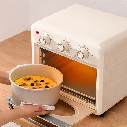 Hands placing a pan with removable handle filled with baked custard and berries into a small countertop oven on a wooden surface.