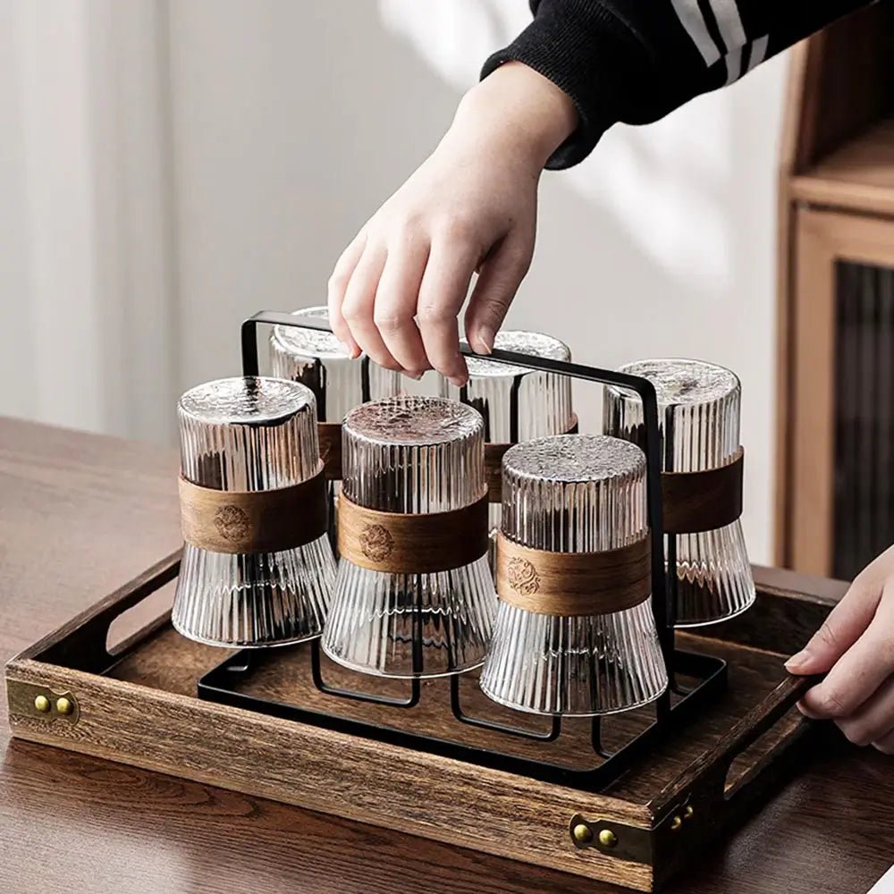 Hand holding metal handle of pitcher and glass set with tray, six ribbed glasses with wooden bands placed upside down
