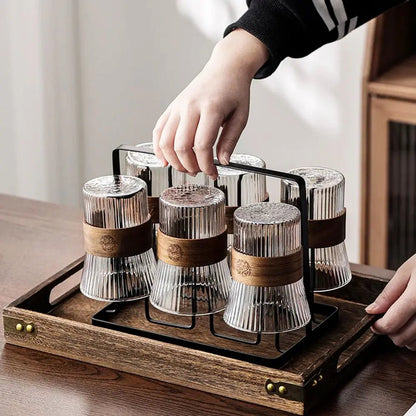 Hand holding metal handle of pitcher and glass set with tray, six ribbed glasses with wooden bands placed upside down