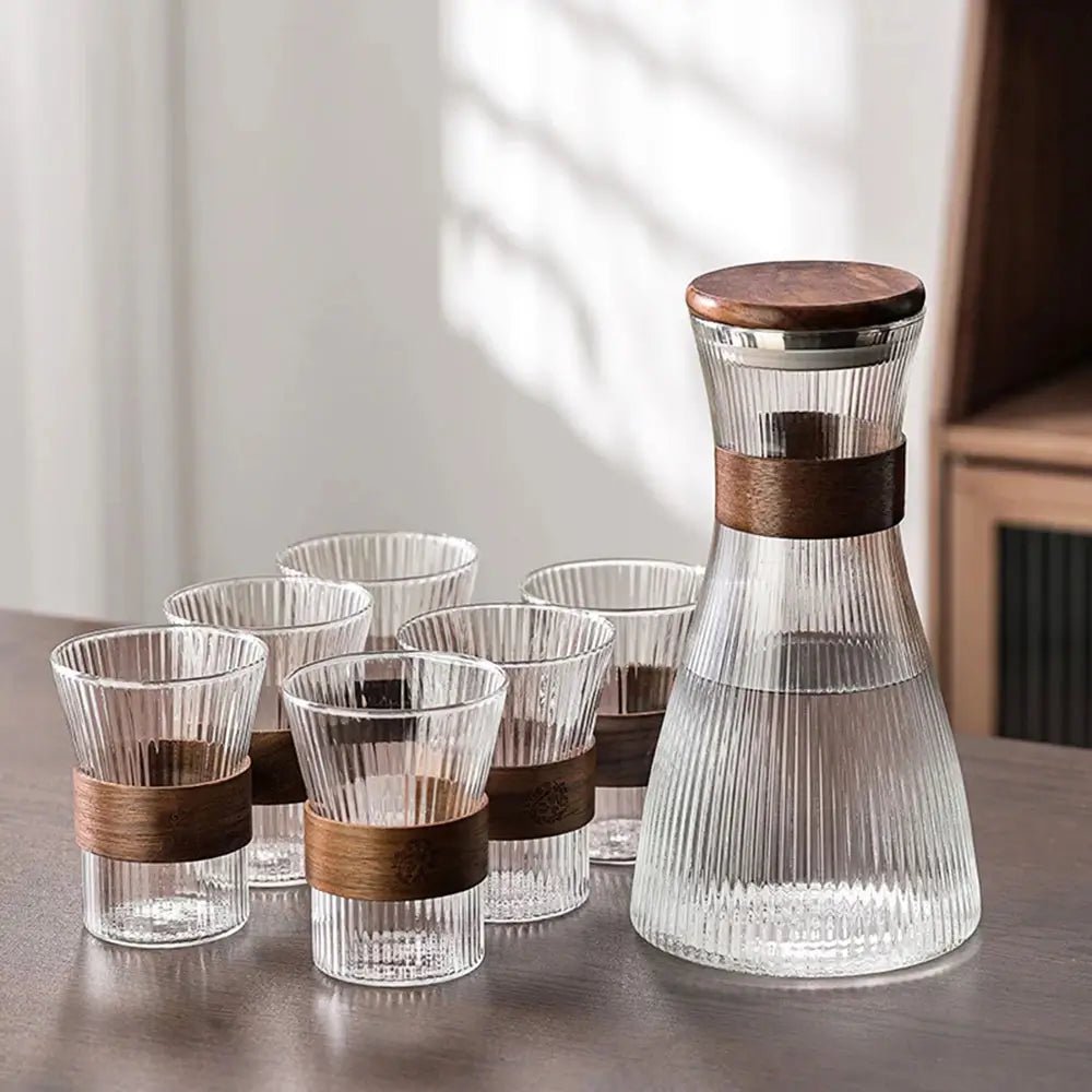 Set of clear glasses with wooden bands and a glass carafe on a table.
